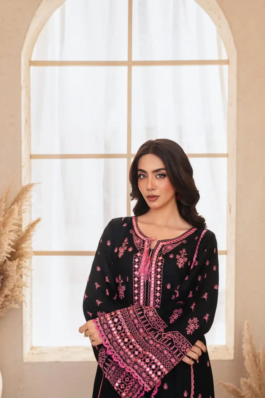 Woman wearing a black and pink embroidered traditional outfit in front of a large window.