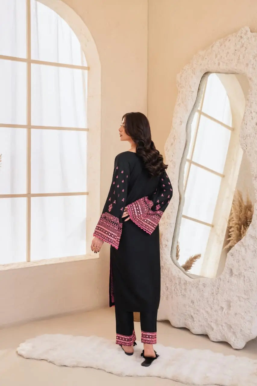 Woman in a black outfit with pink patterns standing in a room with large windows and a decorative mirror.